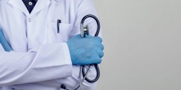 Doctor crossing arms while holding stethoscope in white coat front view.